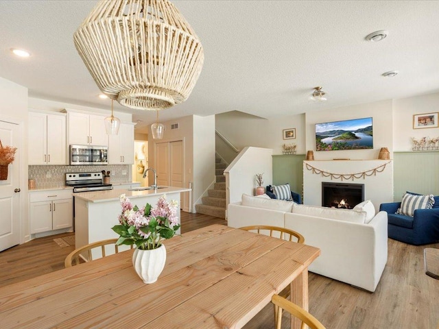 dining space featuring a textured ceiling, stairway, a warm lit fireplace, recessed lighting, and light wood-style flooring