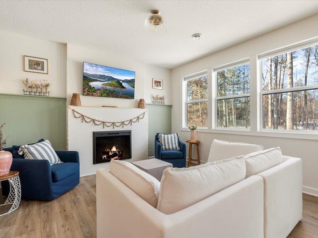 living room with a textured ceiling, a lit fireplace, and wood finished floors