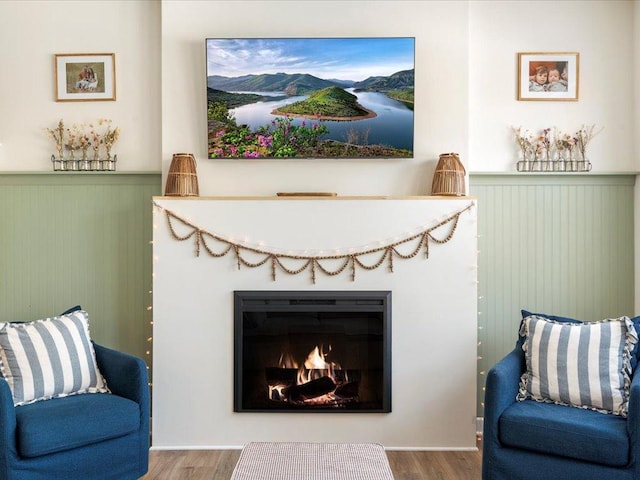 sitting room featuring wood walls, wainscoting, wood finished floors, and a lit fireplace