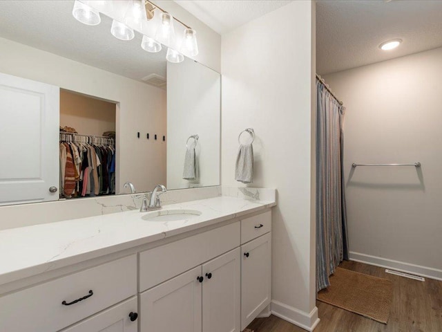 full bathroom featuring vanity, baseboards, wood finished floors, a spacious closet, and visible vents