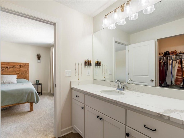 ensuite bathroom with a walk in closet, vanity, a textured ceiling, baseboards, and ensuite bathroom