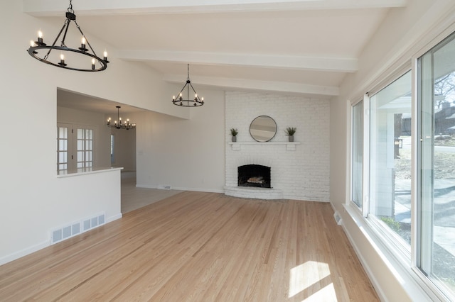 unfurnished living room featuring plenty of natural light, visible vents, light wood-type flooring, and a notable chandelier