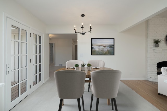 dining space featuring a brick fireplace, baseboards, an inviting chandelier, and light wood-style flooring