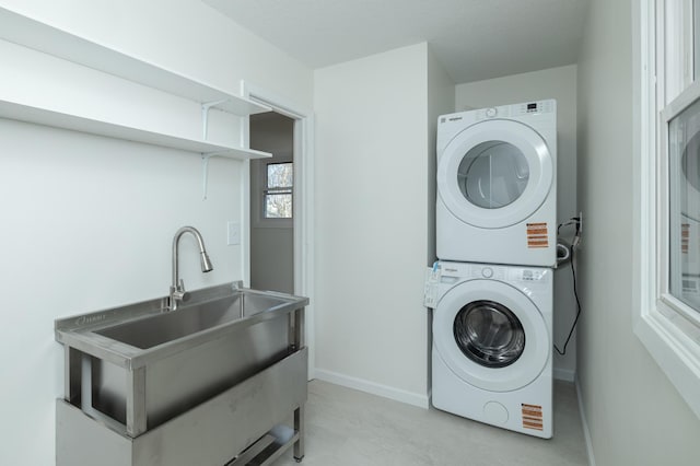 laundry area featuring laundry area, a sink, baseboards, and stacked washer / drying machine