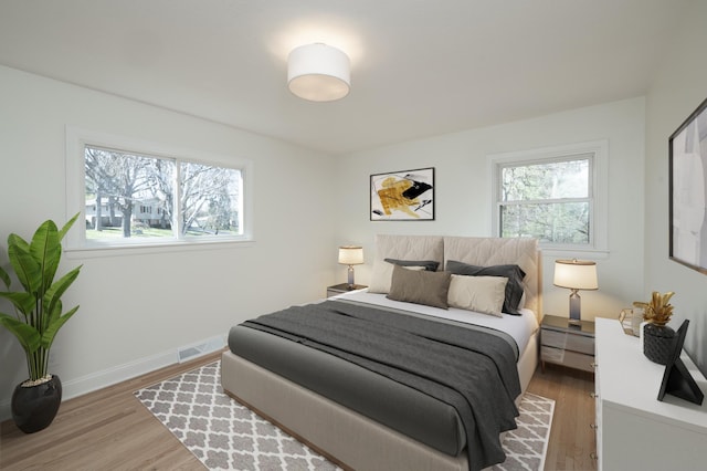 bedroom with visible vents, baseboards, wood finished floors, and multiple windows