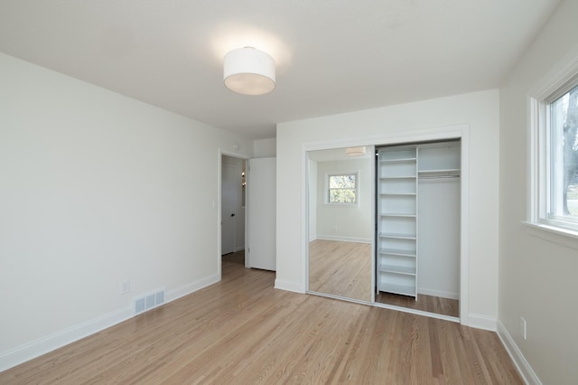 unfurnished bedroom with multiple windows, a closet, light wood finished floors, and visible vents