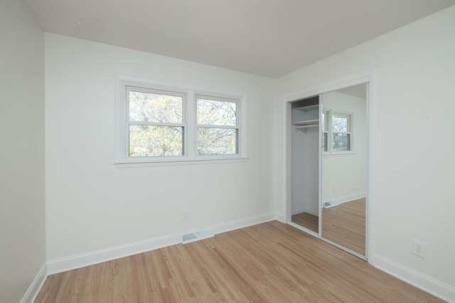 unfurnished bedroom featuring baseboards, visible vents, multiple windows, and light wood-style flooring