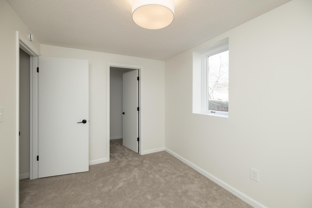unfurnished bedroom featuring baseboards, carpet flooring, a textured ceiling, and a walk in closet