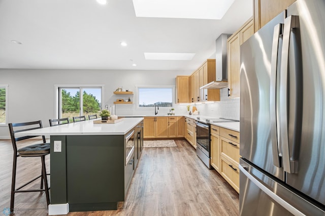 kitchen featuring open shelves, light brown cabinets, wall chimney exhaust hood, appliances with stainless steel finishes, and a skylight