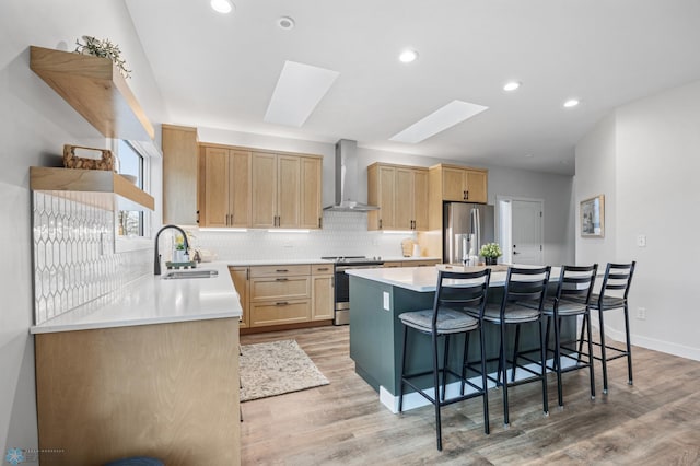 kitchen featuring appliances with stainless steel finishes, a sink, light wood-style flooring, wall chimney exhaust hood, and a skylight