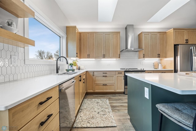 kitchen featuring light brown cabinetry, appliances with stainless steel finishes, a sink, wall chimney exhaust hood, and light wood-type flooring