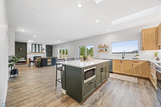 kitchen with decorative backsplash, light wood-style floors, a sink, a skylight, and stainless steel appliances