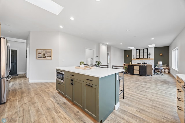 kitchen with light countertops, a kitchen breakfast bar, stainless steel appliances, a skylight, and a center island with sink
