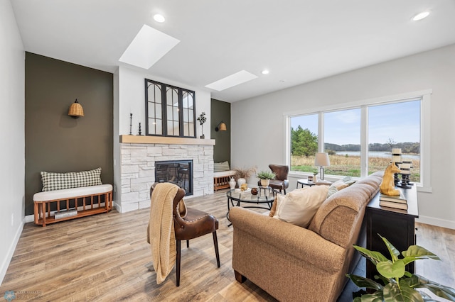 living area featuring a stone fireplace, light wood-style flooring, recessed lighting, baseboards, and a skylight
