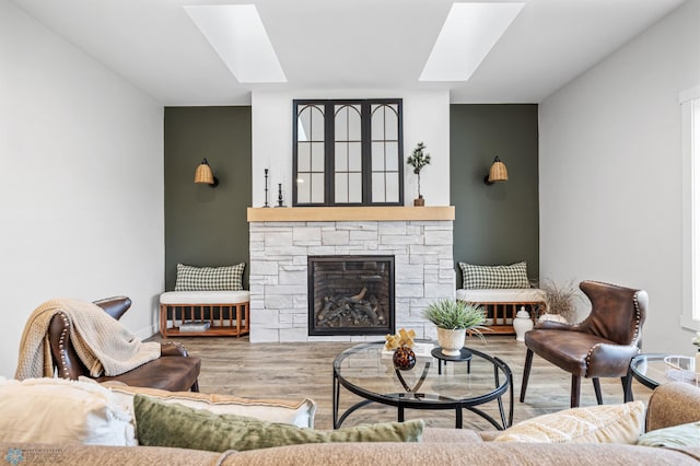 living room with baseboards, a skylight, a stone fireplace, and wood finished floors