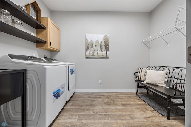 clothes washing area with cabinet space, baseboards, washer and clothes dryer, and light wood-type flooring