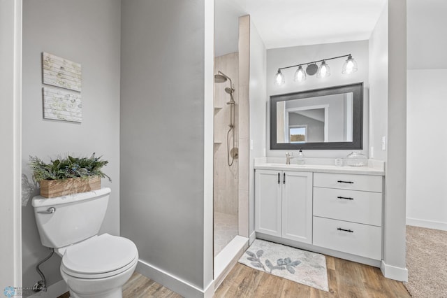 full bathroom with toilet, a tile shower, wood finished floors, and vanity