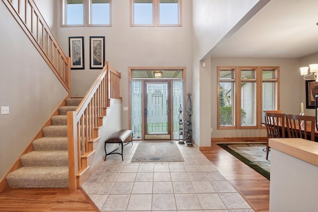foyer with a notable chandelier, baseboards, wood finished floors, a towering ceiling, and stairway