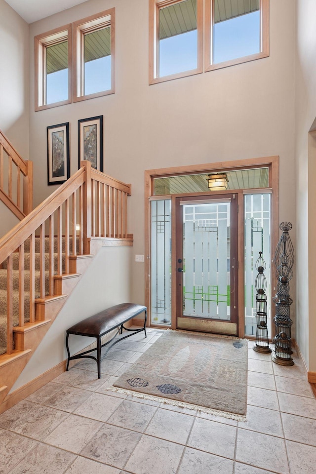 entrance foyer featuring stairs, a high ceiling, baseboards, and stone tile flooring