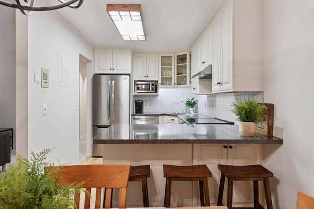 kitchen featuring appliances with stainless steel finishes, tasteful backsplash, a sink, a peninsula, and glass insert cabinets