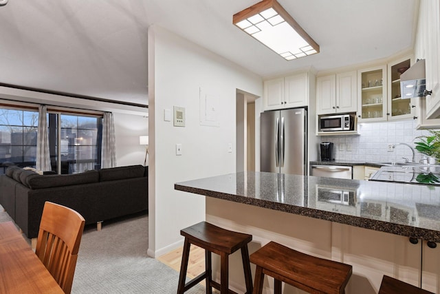 kitchen with a sink, a kitchen breakfast bar, stainless steel appliances, a peninsula, and glass insert cabinets