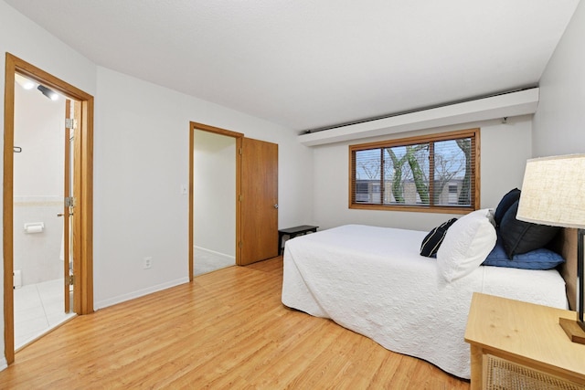 bedroom featuring baseboards, ensuite bathroom, and light wood finished floors