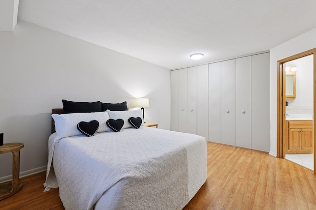bedroom featuring connected bathroom, baseboards, and light wood-style floors