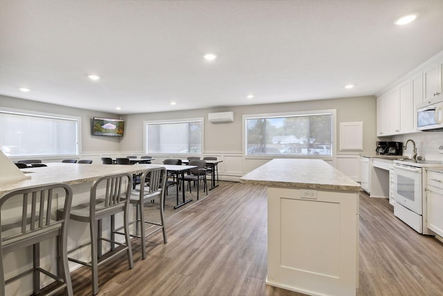 kitchen featuring a kitchen island, wainscoting, light wood-type flooring, light countertops, and white appliances