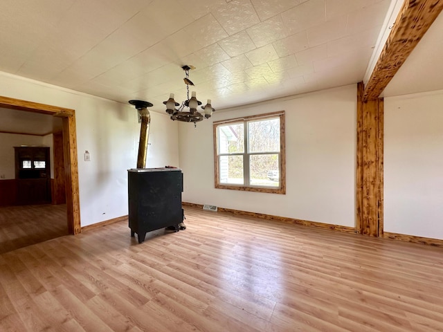 27227 Raven Rd, Spring Valley, MN 55975 - unfurnished living room featuring visible vents, a wood stove, light wood-style floors, baseboards, and a notable chandelier