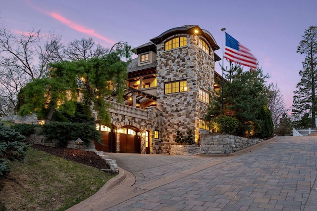 view of front of house with driveway, fence, a balcony, an attached garage, and stone siding