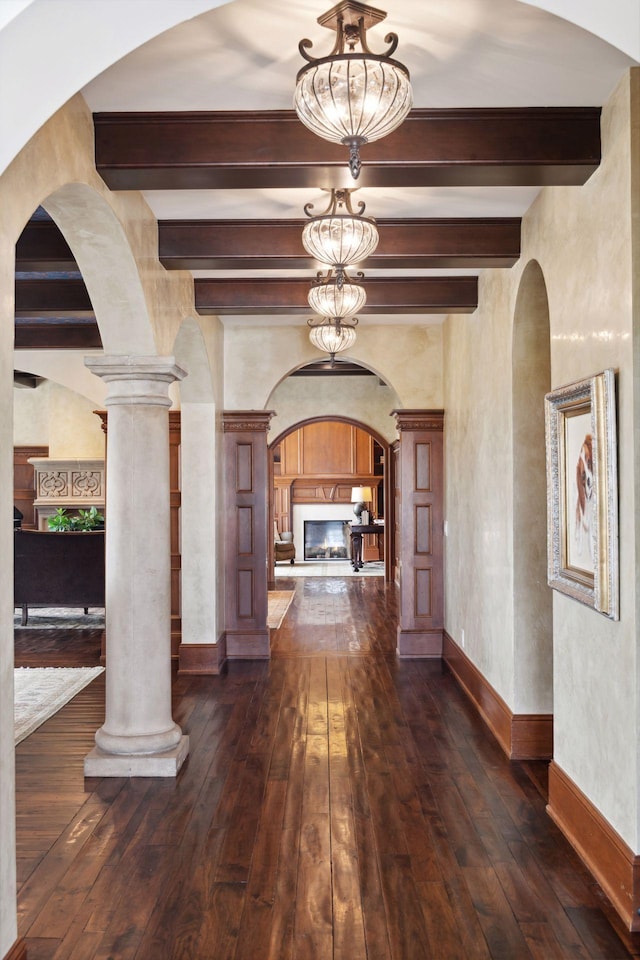 foyer featuring baseboards, beamed ceiling, arched walkways, and dark wood-type flooring