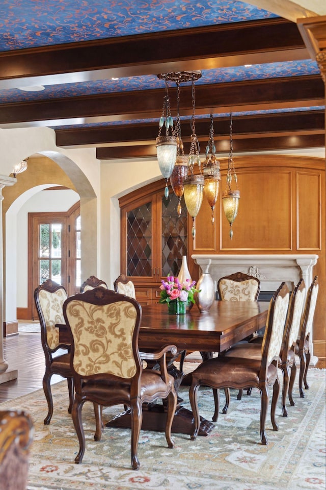 dining area featuring arched walkways, beam ceiling, and light wood-style flooring
