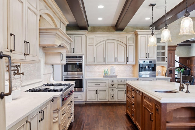 kitchen featuring pendant lighting, appliances with stainless steel finishes, a sink, beamed ceiling, and dark wood-type flooring