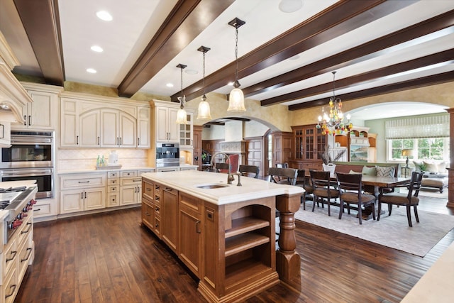 kitchen with a sink, double oven, light countertops, arched walkways, and dark wood-type flooring