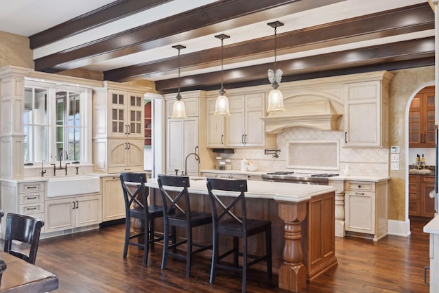kitchen with dark wood-style flooring, an island with sink, light countertops, tasteful backsplash, and a sink