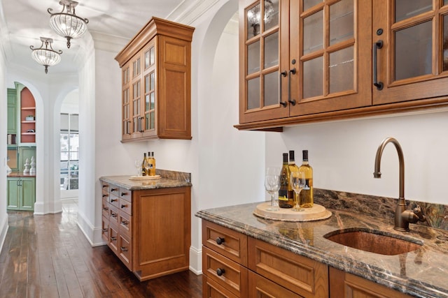 bar featuring ornamental molding, a sink, dark wood-style flooring, baseboards, and arched walkways