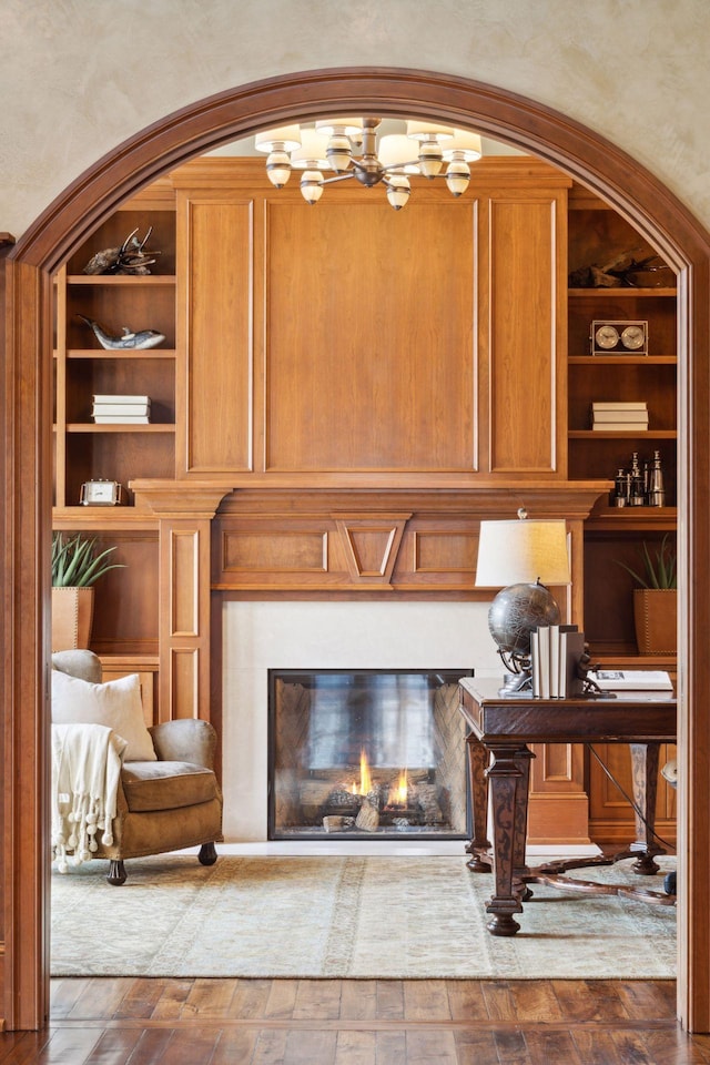 details with a glass covered fireplace, built in shelves, and wood finished floors