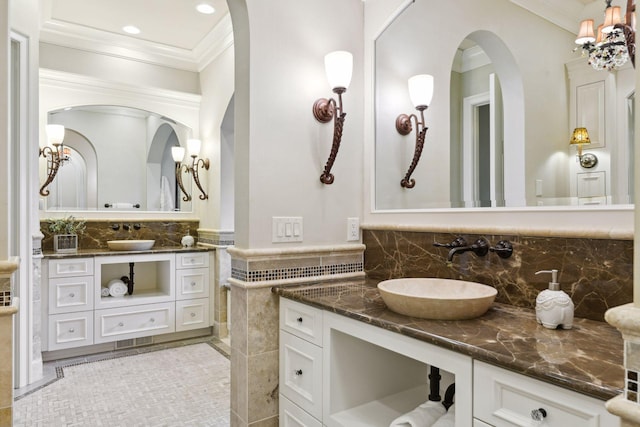 bathroom featuring crown molding, decorative backsplash, two vanities, and a sink