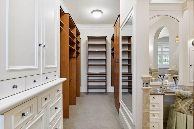 walk in closet with arched walkways and light carpet