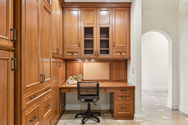 office area featuring baseboards, arched walkways, and built in desk