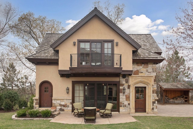 back of property featuring a balcony, stone siding, and stucco siding