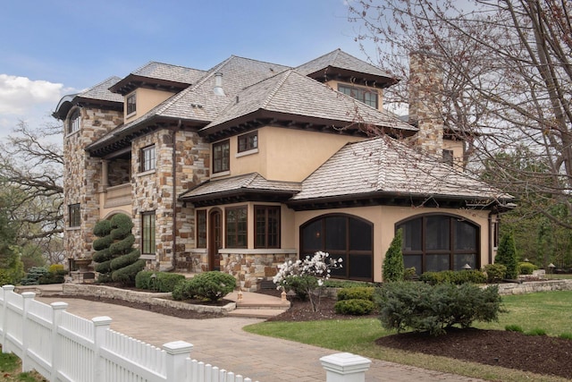 view of front of house featuring stucco siding, stone siding, and fence