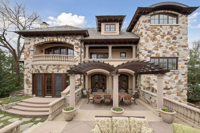 rear view of property featuring a balcony, stone siding, french doors, a chimney, and a patio area
