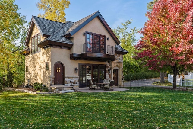 back of house featuring fence, stone siding, stucco siding, a balcony, and a yard