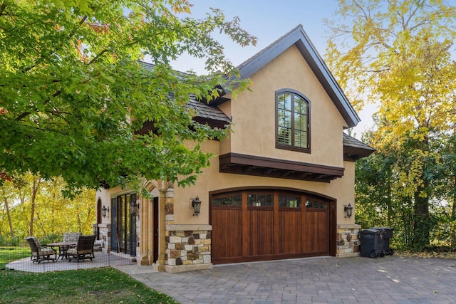 rear view of house with a garage, stucco siding, driveway, and stone siding