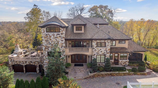 french country inspired facade featuring driveway, a chimney, fence, stone siding, and stucco siding