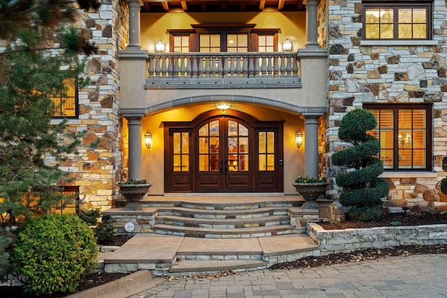 doorway to property featuring a porch, a balcony, and stone siding