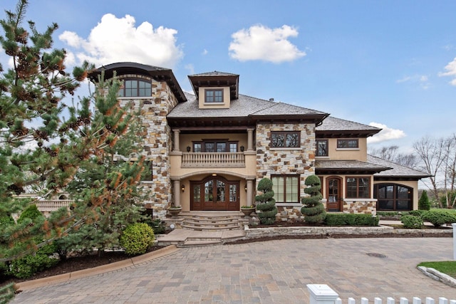 view of front facade featuring stone siding, stucco siding, a sunroom, a balcony, and french doors