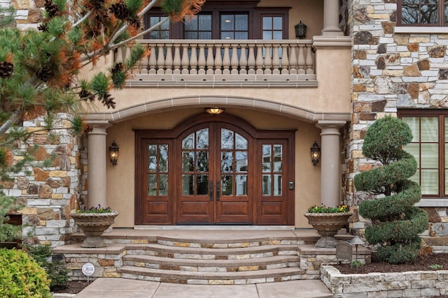 property entrance with a balcony, stone siding, and stucco siding