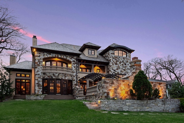 back of house featuring a yard, a high end roof, a balcony, and stone siding